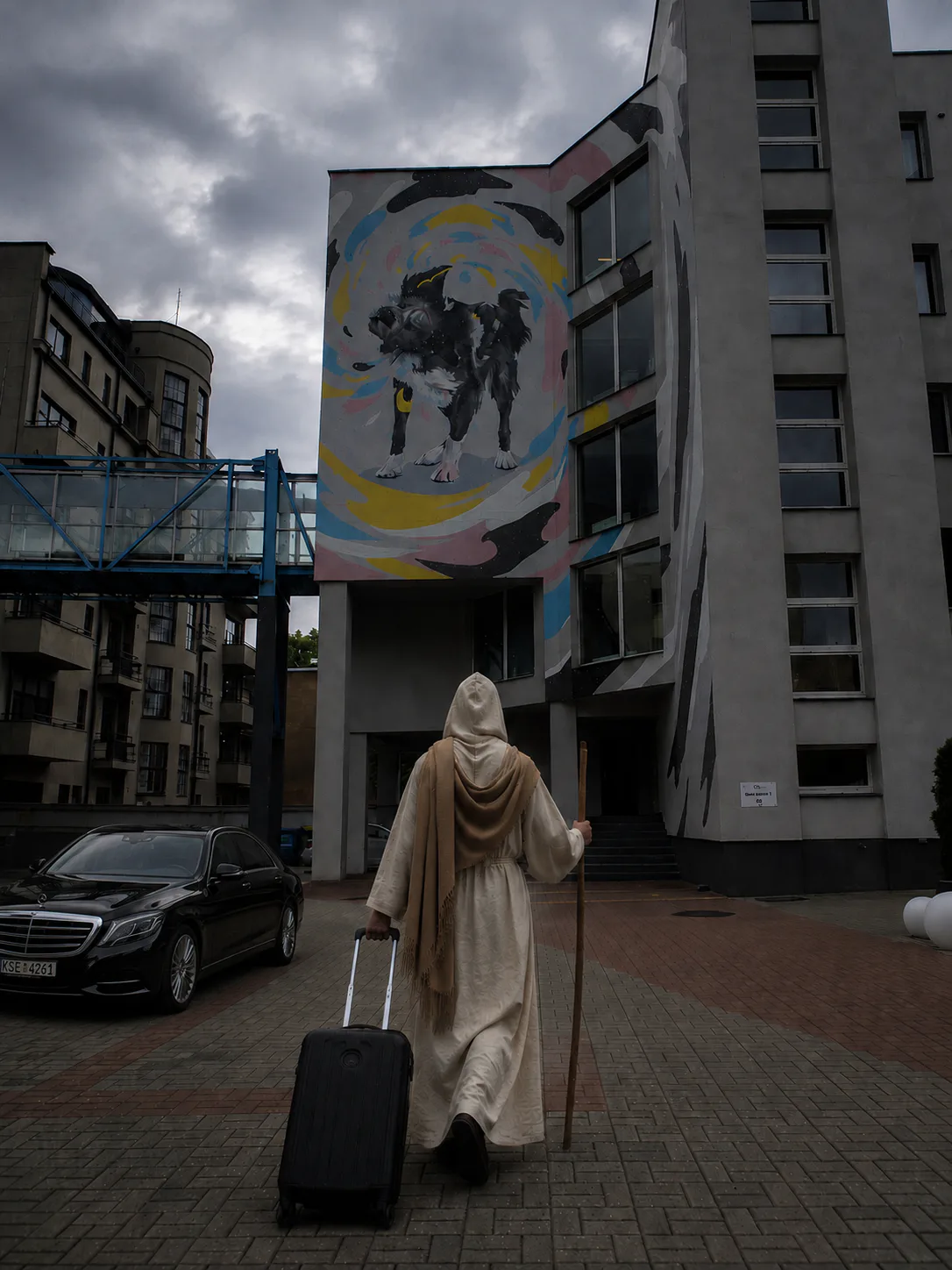 La figura encapuchada llegando con bastón y maleta a un edificio de Kaunas